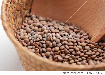 Uncooked brown lentil grains in woven basket with rustic spoon. Traditional raw ingredient of Mediterranean cuisine. Macro shot Uncooked brown lentil grains in woven basket with rustic spoon. Traditional raw ingredient of Mediterranean cuisine. Macro shot 136363847