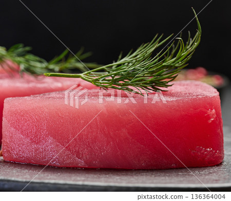 Raw piece of tuna with a sprig of dill on a black board, close up Raw piece of tuna with a sprig of dill on a black board, close up 136364004
