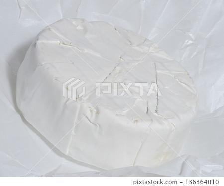A round head of Camembert cheese lies on white parchment paper. A round head of Camembert cheese lies on white parchment paper. 136364010