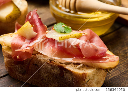 Italian bruschetta with prosciutto, pear slices, cream cheese and fresh basil, garnished with sesame seeds Italian bruschetta with prosciutto, pear slices, cream cheese and fresh basil, garnished with sesame seeds 136364050