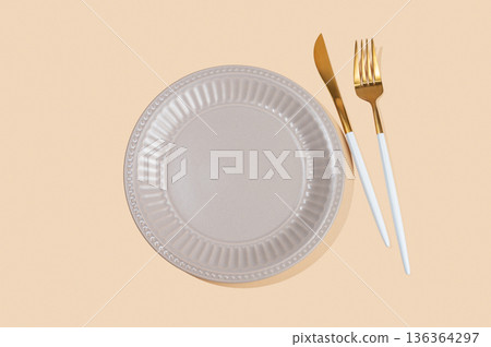 A ceramic beige plate with a cutlery on a yellow isolated background. A ceramic beige plate with a cutlery on a yellow isolated background. 136364297