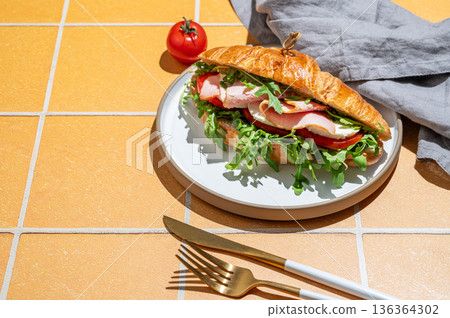 Croissant sandwich with ham, mozzarella cheese and arugula on a plate on a yellow tile background 136364302