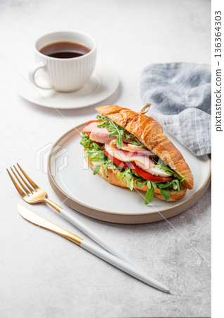 Croissant sandwich with ham, cheese, tomato, arugula on a plate and cup of coffee 136364303