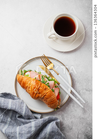 Croissant sandwich with ham, mozzarella cheese, tomato, arugula on a plate and cup of coffee Croissant sandwich with ham, mozzarella cheese, tomato, arugula on a plate and cup of coffee 136364304