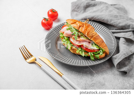 Croissant sandwich with ham, mozzarella cheese and arugula on a plate on a light background 136364305