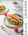 Croissant sandwich with ham, mozzarella cheese, tomato, arugula on a plate and cup of coffee 136364306