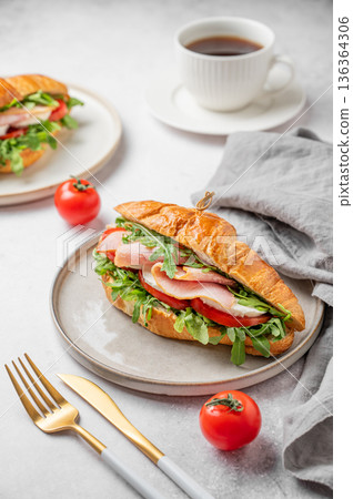 Croissant sandwich with ham, mozzarella cheese, tomato, arugula on a plate and cup of coffee Croissant sandwich with ham, mozzarella cheese, tomato, arugula on a plate and cup of coffee 136364306