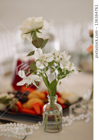 White flowers in small glass vase on table in classic room with blurred background 136364761