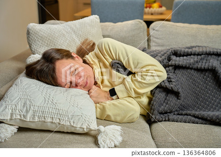 Woman sleeping on sofa with pillow and blanket in home interior Woman sleeping on sofa with pillow and blanket in home interior 136364806