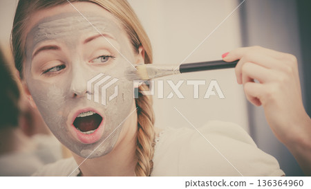 Woman applying with brush clay mud mask to her face Woman applying with brush clay mud mask to her face 136364960