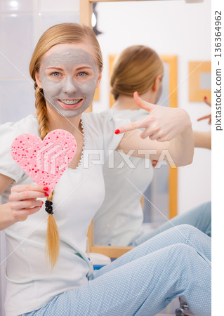 Woman having grey face mask holding heart sponge 136364962