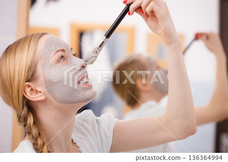 Woman applying with brush clay mud mask to her face Woman applying with brush clay mud mask to her face 136364994