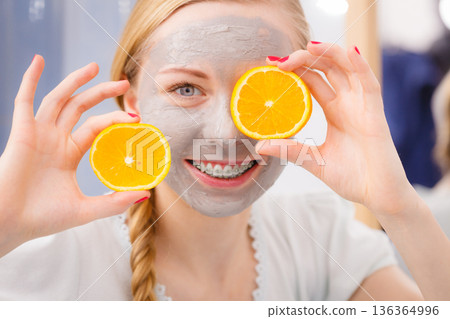 Happy young woman having face mask holding kiwi Happy young woman having face mask holding kiwi 136364996