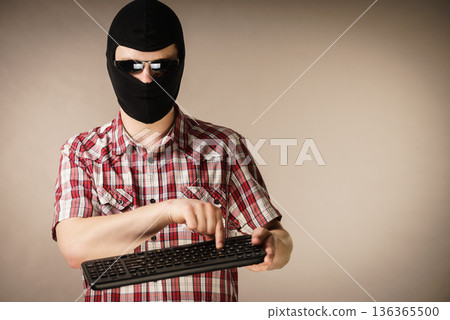 Man wearing balaclava holding keyboard 136365500