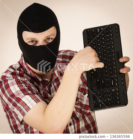 Man wearing balaclava holding keyboard 136365506