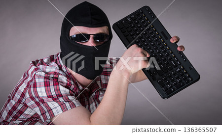 Man wearing balaclava holding keyboard 136365507