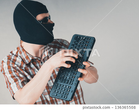 Man wearing balaclava holding keyboard 136365508