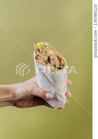 Hand holding grilled pork wrap with greens on green background 136366128