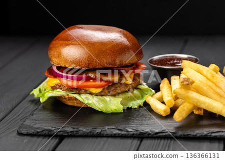 Beef cheeseburger with lettuce, tomato and onion, served with fries and ketchup on slate board 136366131