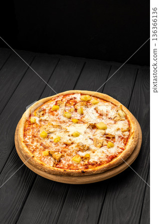 Chicken pineapple pizza with melted mozzarella on wooden board, dark background Chicken pineapple pizza with melted mozzarella on wooden board, dark background 136366136