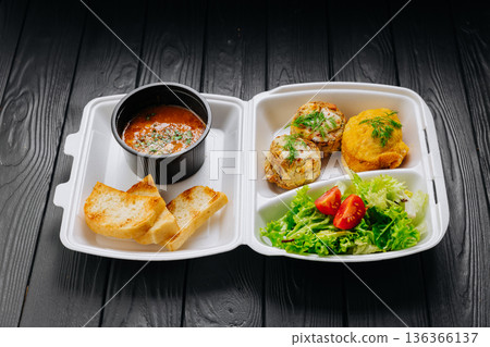 Takeaway lunch box with tomato soup, salad and cutlets on dark wooden table Takeaway lunch box with tomato soup, salad and cutlets on dark wooden table 136366137
