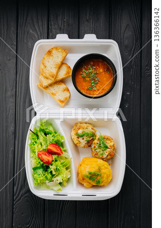 Takeaway lunch box with tomato soup, salad and cutlets on dark wooden table Takeaway lunch box with tomato soup, salad and cutlets on dark wooden table 136366142