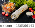Whole shawarma wrap with fries and dipping sauces on black table 136366143
