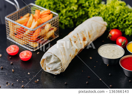 Whole shawarma wrap with fries and dipping sauces on black table Whole shawarma wrap with fries and dipping sauces on black table 136366143