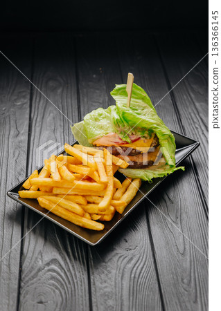 Bunless beef burger in lettuce wrap with fries on black plate, copy space Bunless beef burger in lettuce wrap with fries on black plate, copy space 136366145