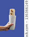 Hand holding wrapped shawarma in paper sleeve isolated on blue background 136366149