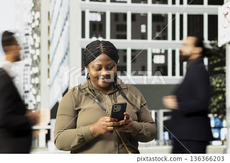 African american female adult browsing phone apps in the metropolitan area, walking among constant urban motion and crowd of pedestrians. Everyday routine and dynamic street life. African american female adult browsing phone apps in the metropolitan area, walking among constant urban motion and crowd of pedestrians. Everyday routine and dynamic street life. 136366203