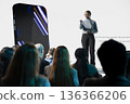 African american girl with microphone introducing new smartphone on stage, release announcement with promotion visuals. Advertising new launch for investment deal during convention event. 136366206