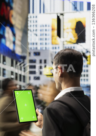 Vertical green screen on tablet with indian adult near busy crosswalk with urban people highlighting different lifestyles, multicultural crowd and everyday street activity in a metropolitan area. Vertical green screen on tablet with indian adult near busy crosswalk with urban people highlighting different lifestyles, multicultural crowd and everyday street activity in a metropolitan area. 136366208