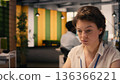 Frowning businesswoman with confused and skeptical expression at desk, appearing uncertain and indecisive reviewing visual data on laptop. Undetermined irregular performance metrics, confusion. 136366221