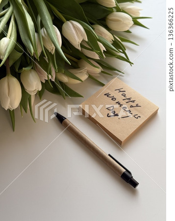 Sticky note with handwritten phrase happy women's day on white office table with pen and tulips flowers bouquet close up 136366225