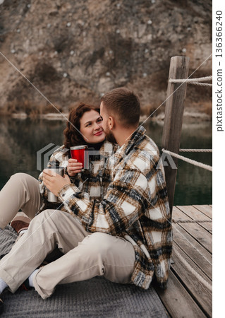 Couple enjoys warm drinks by the lakeside on Valentines Day while dressed in cozy outfits Couple enjoys warm drinks by the lakeside on Valentines Day while dressed in cozy outfits 136366240