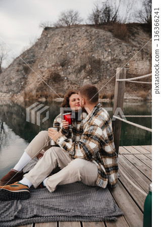 Couple enjoys hot drinks on a dock near water during a chilly afternoon in winter 136366241