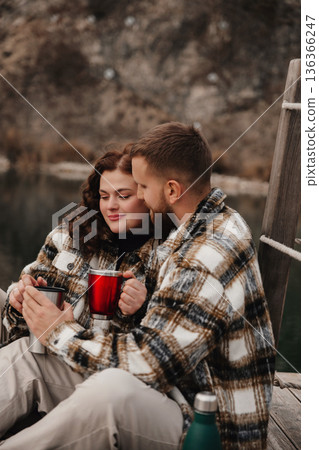 Couple enjoying warm drinks by the water on Valentines Day while wearing matching outfits in winter Couple enjoying warm drinks by the water on Valentines Day while wearing matching outfits in winter 136366247