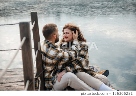 Couple sitting on wooden dock by water sharing moments on a cloudy day 136366281
