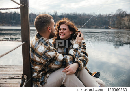 Couple sits by the water on a cold day enjoying each others company and celebrating love together 136366283