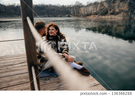 Couple enjoys a quiet moment together by the water on Valentines Day while sitting on a wooden dock 136366288