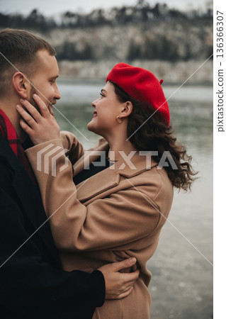 Couple enjoys a romantic moment by the water on Valentines Day wearing warm clothes and sharing smiles in nature 136366307