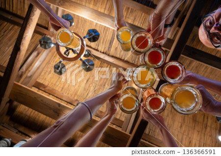 Berlin, germany, august 12, 2023. Friends raising beer glasses in a lively pub toast, clinking mugs and sharing joyful, casual moments of celebration and togetherness Berlin, germany, august 12, 2023. Friends raising beer glasses in a lively pub toast, clinking mugs and sharing joyful, casual moments of celebration and togetherness 136366591