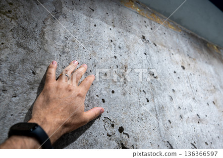 Berlin, germany, august 12, 2023. Hand feeling coarse, weathered concrete wall texture in outdoor sunlight, close-up showing rough gray surface, shadow and detail Berlin, germany, august 12, 2023. Hand feeling coarse, weathered concrete wall texture in outdoor sunlight, close-up showing rough gray surface, shadow and detail 136366597