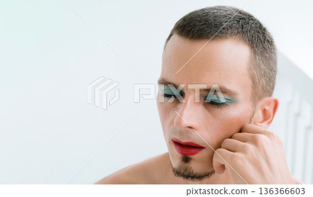 portrait of a feminine young gay man with makeup and cosmetics on face. A handsome transgender male with red lipstick on lips and mascara on eyes portrait of a feminine young gay man with makeup and cosmetics on face. A handsome transgender male with red lipstick on lips and mascara on eyes 136366603