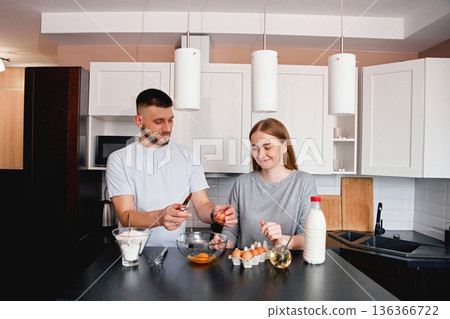 Couple prepares breakfast in a modern kitchen while cracking eggs and mixing ingredients for a meal Couple prepares breakfast in a modern kitchen while cracking eggs and mixing ingredients for a meal 136366722