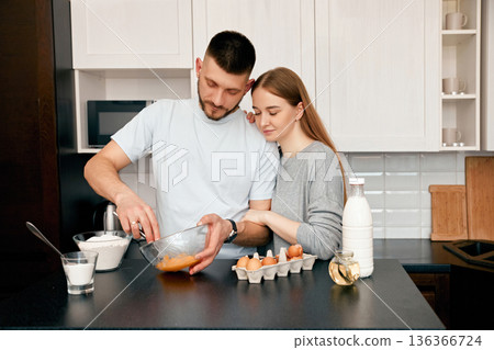 Couple cooks together in kitchen preparing breakfast with eggs and milk during morning hours Couple cooks together in kitchen preparing breakfast with eggs and milk during morning hours 136366724