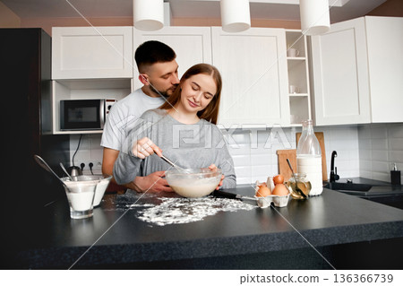 Couple prepares food together in home kitchen while mixing ingredients and sharing a moment in the morning light 136366739