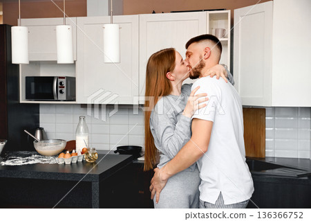 Couple sharing a kiss while cooking together in a modern kitchen during the morning hours 136366752