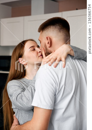 Couple shares a kiss in a modern kitchen during a cozy afternoon at home with natural light shining through the windows Couple shares a kiss in a modern kitchen during a cozy afternoon at home with natural light shining through the windows 136366754